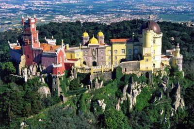La ciudad de Sintra est&aacute; toda engalanada de mansiones y palacios -como el de Pena- edificados por los muchos reyes, arist&oacute;cratas, millonarios y artistas que a lo largo de su historia cayeron rendidos ante la belleza de este paraje natural, descolgado por una frondosa sierra de granito surcada de precipicios y manantiales. Retiro predilecto de los monarcas portugueses, el conjunto de Sintra, ciudad, sierra y paisajes est&aacute; declarado Patrimonio de la Humanidad por la Unesco.